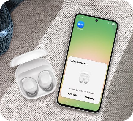 Vemos um par de Galaxy Buds Core branco em seu estojo de carregamento ao lado de um smartphone Samsung Galaxy com o pop-up de pareamento exibido na tela.
