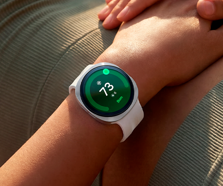 Uma pessoa deitada de costas está usando um Galaxy Watch9 na cor Prata com Pulseira Sport na cor Branco no pulso, mostrando a capacidade de monitoramento da saúde do coração do Galaxy Watch9.