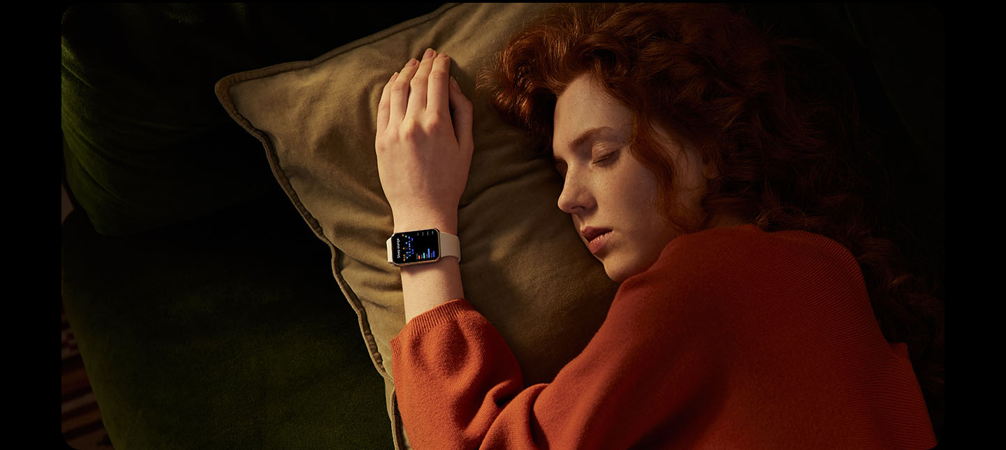 Vemos um Galaxy Fit3 exibindo a tela de detecção de queda em close-up, perguntando 'Precisa de ajuda?' com um botão de chamada SOS e um botão de cancelamento.