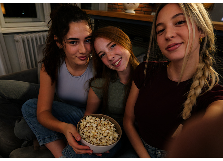 Três jovens estão sentadas em um sofá em casa, em um ambiente com pouca luz, tirando uma foto juntas. Uma delas tira a foto usando o Galaxy A37 5G com Nightography para registrar detalhes mais brilhantes e vibrantes.