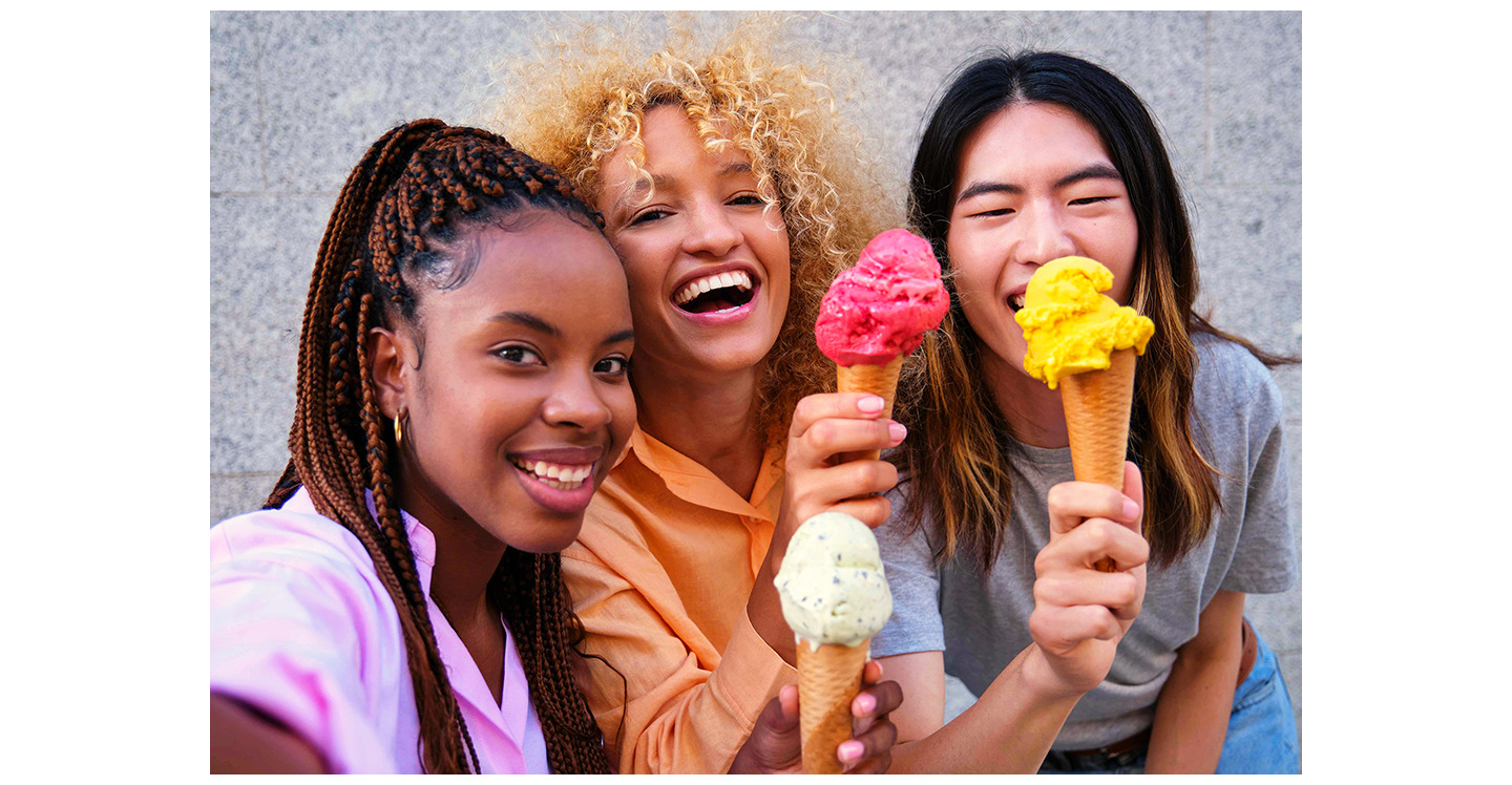 Três jovens, em pé e bem próximas, estão sorrindo e segurando casquinhas de sorvete enquanto tiram uma selfie. Uma delas tira a selfie usando a Câmera Frontal do Galaxy A37 5G para capturar detalhes vibrantes e nítidos.