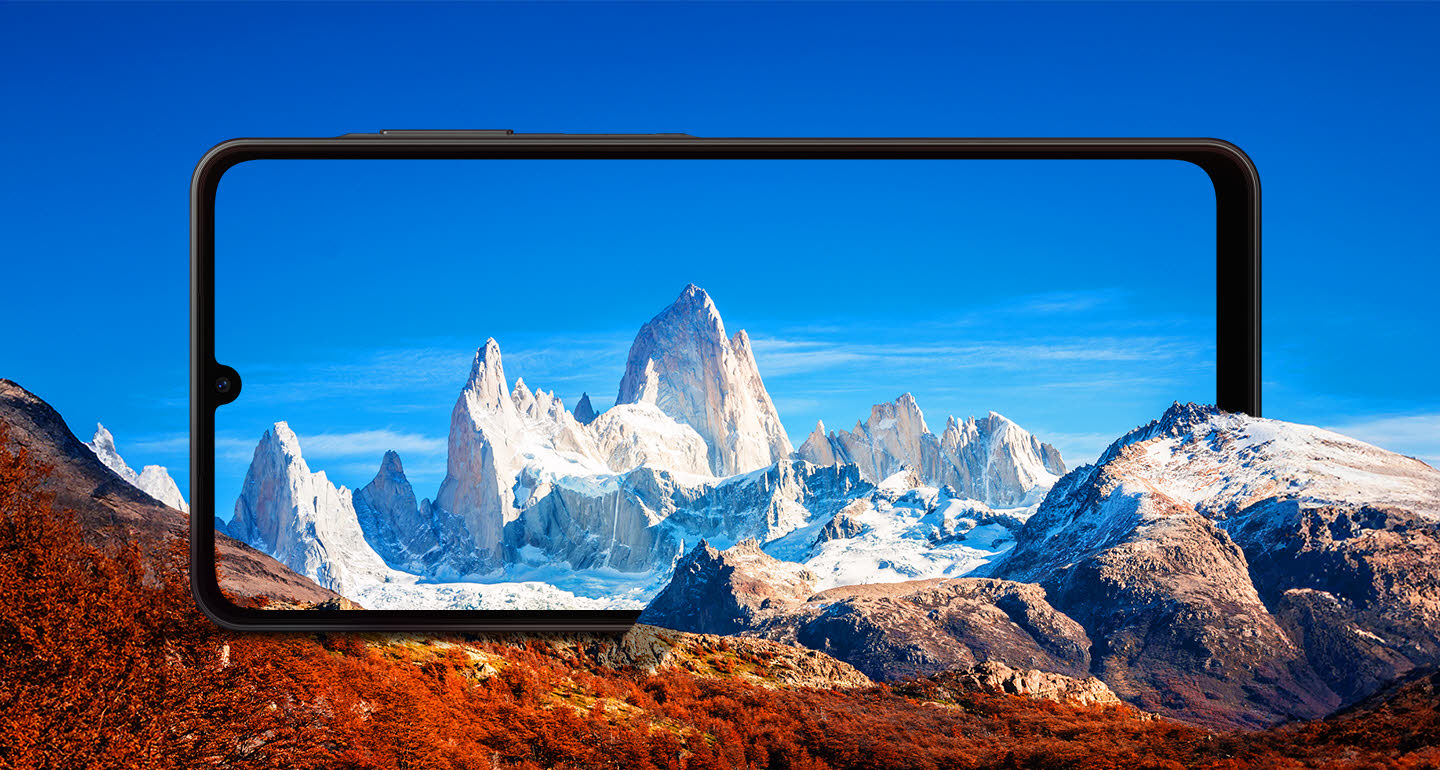 Um Galaxy A06 5G é posicionado horizontalmente entre montanhas rochosas. A tela enquadra montanhas com neve ao fundo contra um céu azul.
