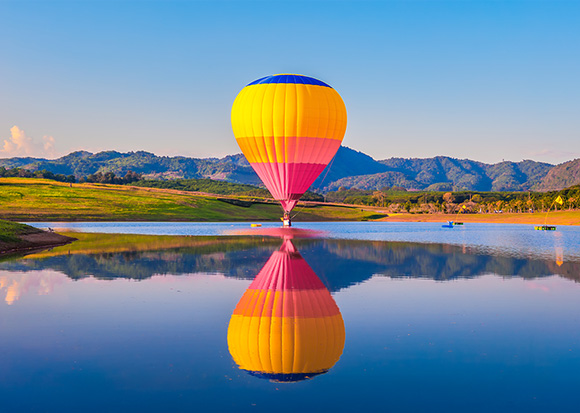 Vemos um colorido balão de ar quente flutuando sobre um lago, refletindo na água.