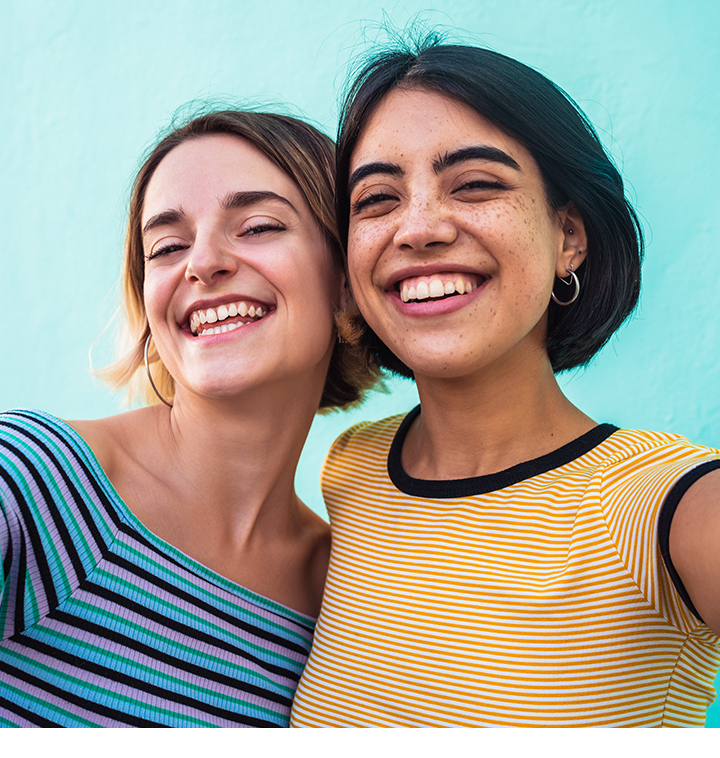 Duas mulheres sorriem enquanto tiram uma selfie juntas usando a Câmera Frontal de 12 MP do Galaxy A27 5G. A selfie tem cores vibrantes, detalhes nítidos e exposição equilibrada, com aparência natural.